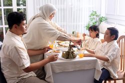 Muslim Woman Serving Foods to Her Husband and Kids in Dining Room While Having Dinner During Eid Mubarak at Home