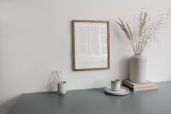 Wooden frame hung above desk with vase branches, books and cup of coffee