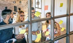 Happy business people in a work meeting placing sticky notes on the wall