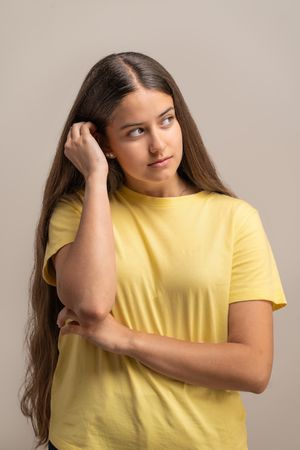 Pensive young woman touching her hair, lost in thought and daydreaming.