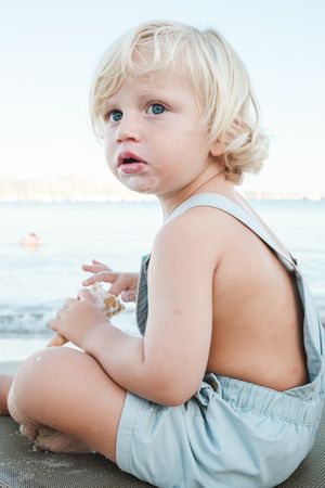 Cute boy sitting on beach while eating ice cream
