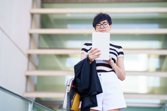 Female in casual outfit and eyeglasses browsing tablet outside building