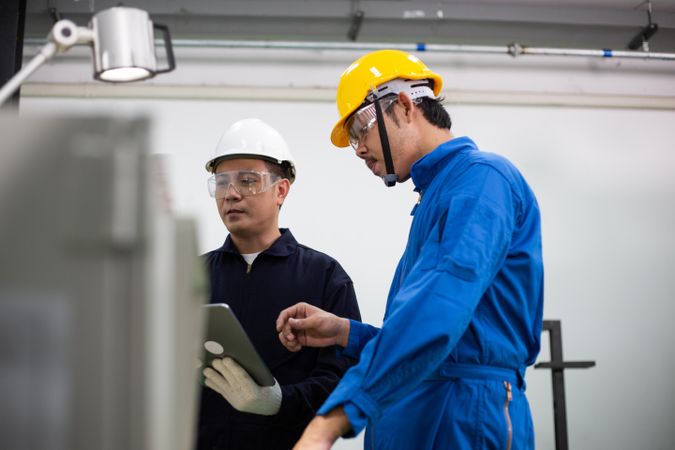 Asian man in blue jumpsuits and hard hats working with industrial machinery