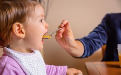 Baby eating puree from a spoon in the hand of mother