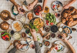 Group of people serving themselves at Turkish style breakfast with eggs, breads, vegetables, tea