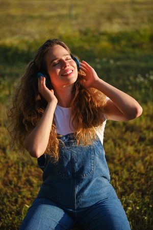 Cheerful woman listening to music in headphones in park