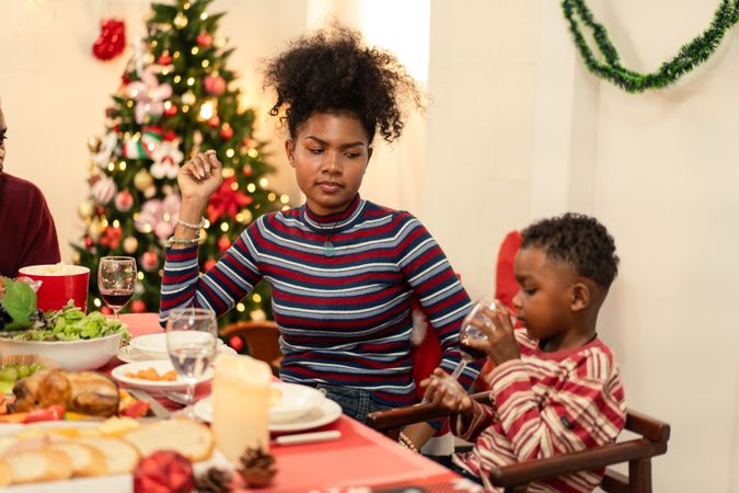 Black family seated Christmas dinner table, small boy drinking,