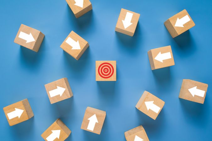 wooden blocks with arrow pointing on target isolated on blue background. concept of goals achievement