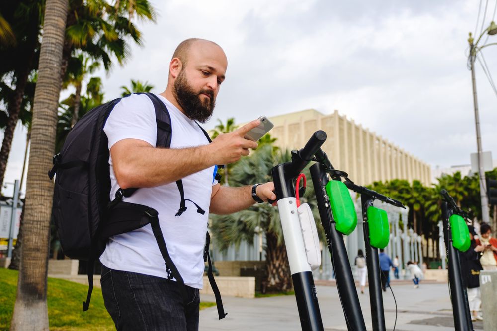 Traveler with backpack browsing smartphone and choosing electronic scooter