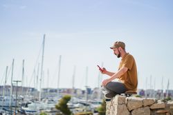 Man in cap relaxed sitting on skateboard using mobile phone