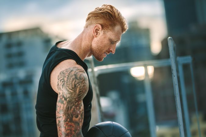 Side view of a fitness person with tattoo on arm doing workout standing  on rooftop