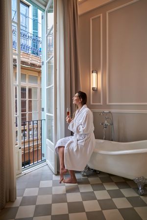 Woman in bathrobe on edge of bathtub champagne glass