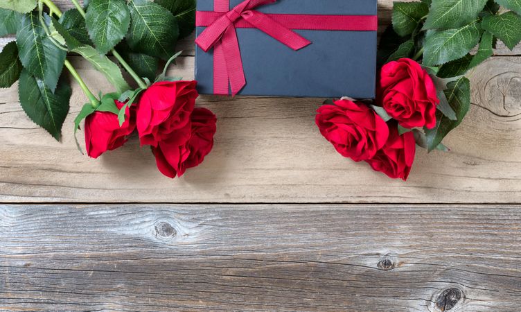 Wrapped gift box with lovely red roses on weathered wood for the seasonal holiday