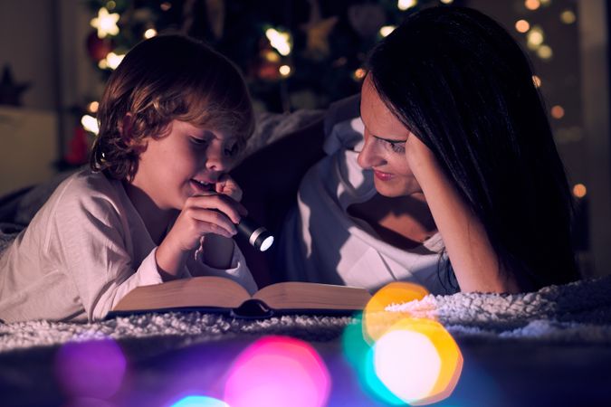 Boy reading book with mother in illuminated room