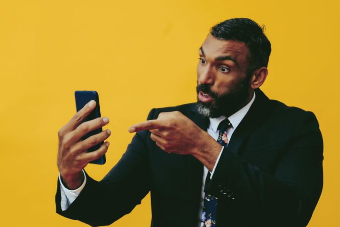 Annoyed Black businessman in suit speaking at smartphone screen while pointing