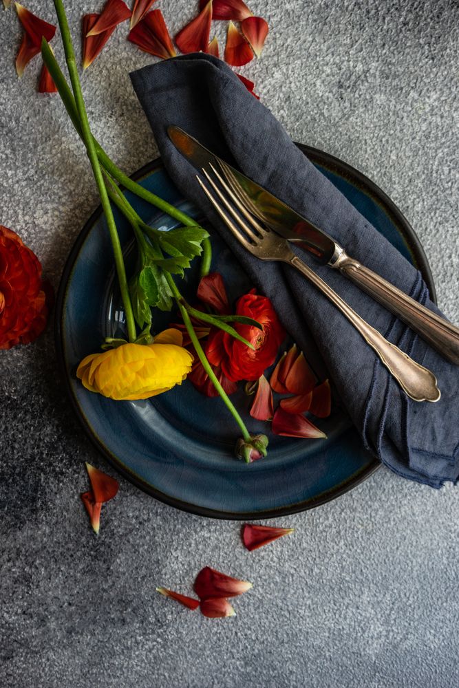 Top view of rustic table setting with red & yellow buttercup flowers on navy plate