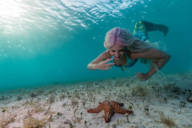 Redhead fairytale female mermaid swimming beside starfish