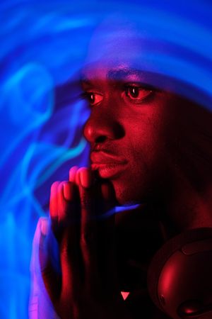 Pensive Black man in headphones on neck in neon illumination