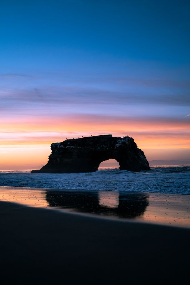 Silhouette of rock in sea during sunset