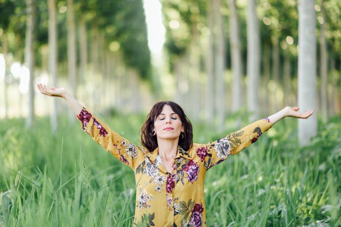 Brunette female in field of tall grass with open arms and eyes closed