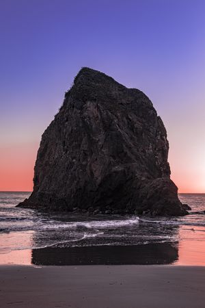 Large rock on the coast at dusk with beautiful purple orange sky, vertical composition