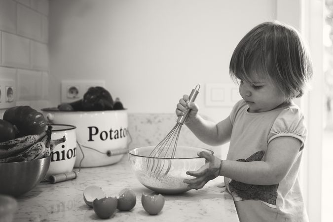 Grayscale photo of toddler mixing eggs in kitchen