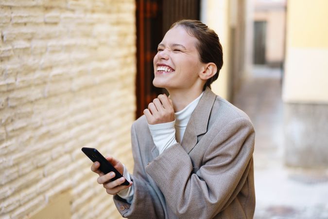 A Joyful Woman Happily Enjoying a Lighthearted Moment with Her Smartphone in a Charming Alleyway