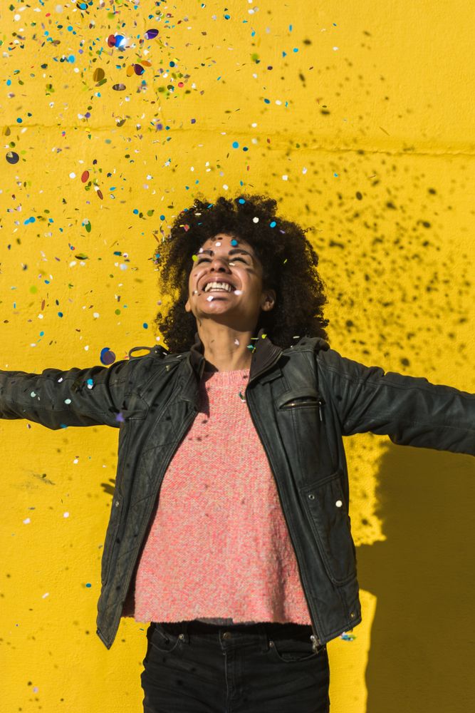 Black woman with afro hair celebrating with confetti.