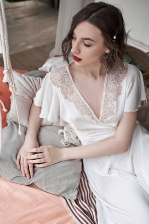 woman with red lips in white dress looking away while sitting on floor beside sofa