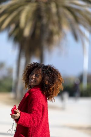 Confident female turning around while listening to music on phone on street with palm trees