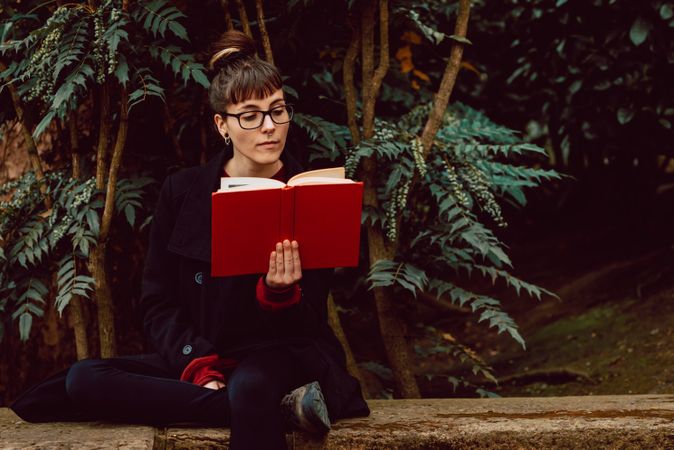 Young woman reading book on bench in park