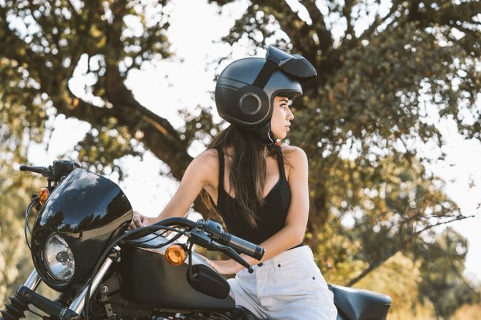 Attentive woman in helmet sitting on parked motorcycle at rural area