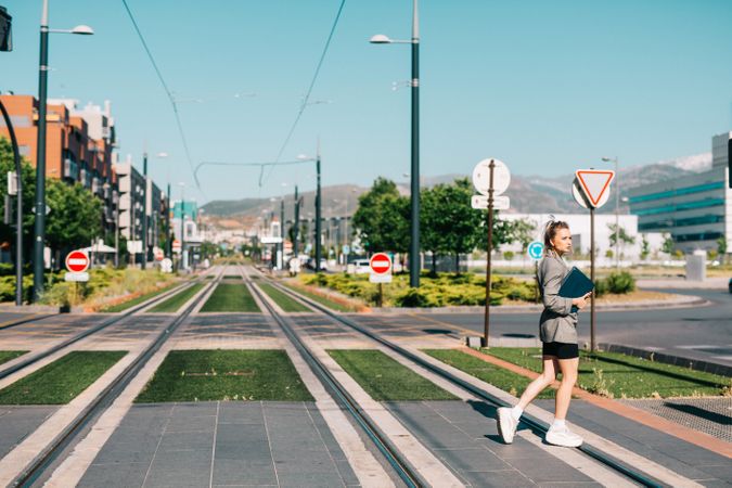 Stylish woman with notebook passing road in city