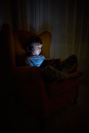 Boy in headphones playing on tablet in darkness