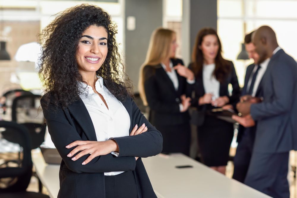 Curly haired business leader standing in foreground of busy office