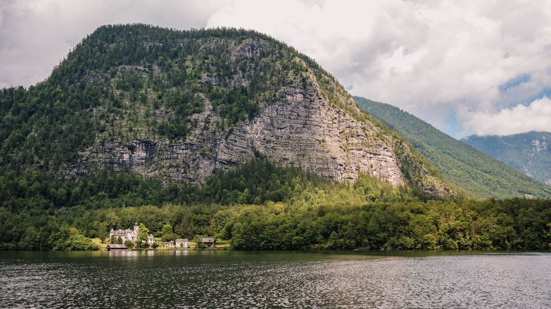A mountain on the shore of the alpine lake Hallstätter See illuminated by the afternoon sun shining through the rain clouds