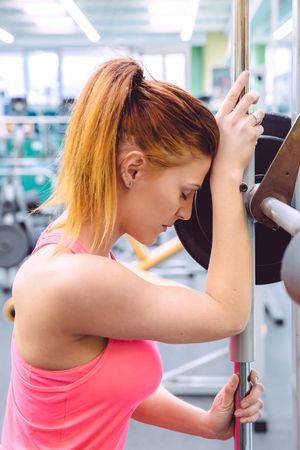 Red haired woman leaning on barbell in between lifting