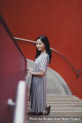 Woman in light and blue dress standing on stairs near red wall 0yGDR4