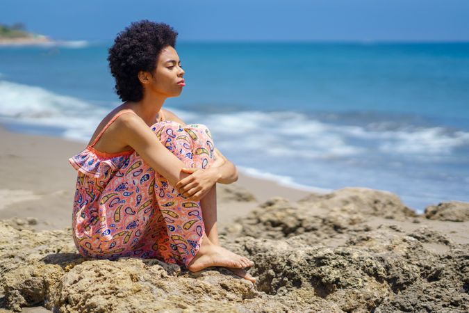 Woman sitting on the rocks on the coast looking out to the sea