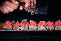 Faceless chef slicing truffle on sushi rolls with tuna