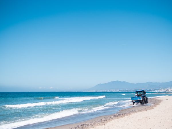 Small tractor riding along sandy seashore