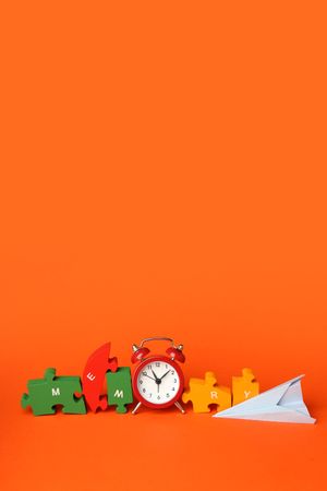 Vertical composition of puzzle pieces spelling “memory” on orange background with alarm clock