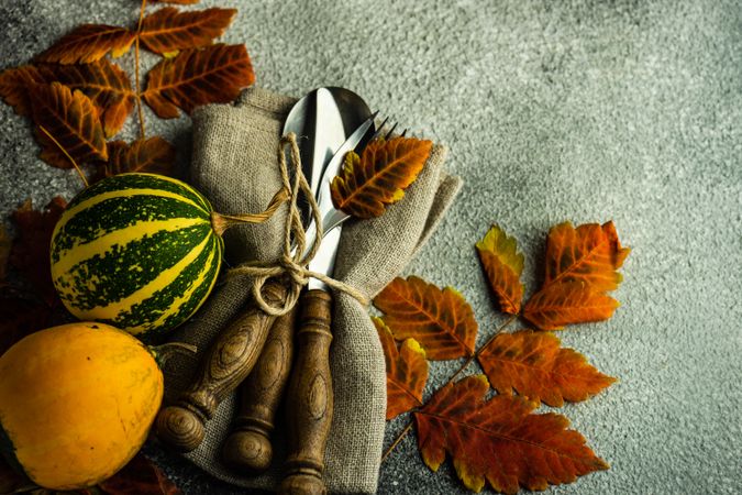 Fall table setting with orange yellow leaves and squash gourds on stone background