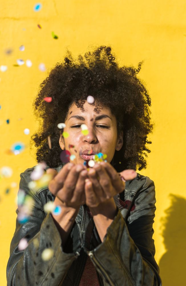 Black woman with afro hair celebrating with confetti.