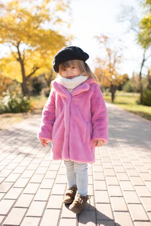 Girl in pink jacket and dark hat standing on sidewalk