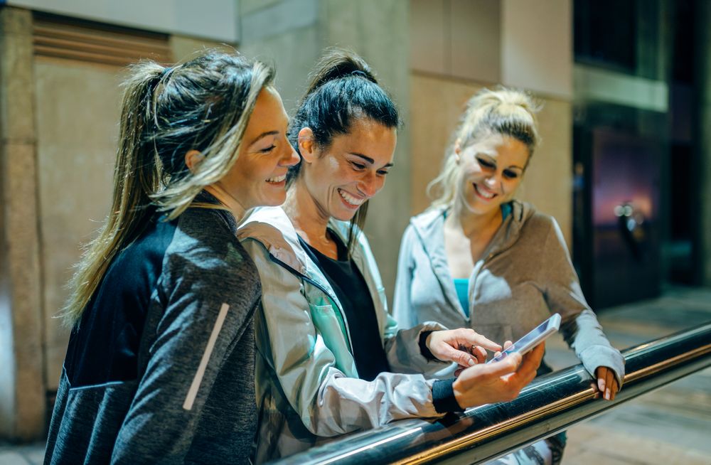 Happy women friends laughing while looking at app together on mobile phone