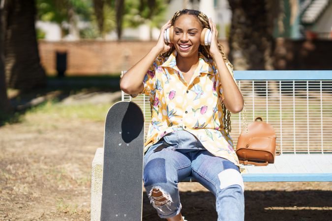 Smiling female in bold patterned shirt on park bench listening to music on large headphones