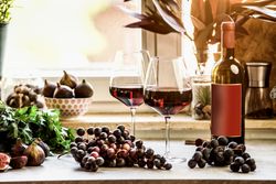 Red wineglasses with grapes and wine bottle at kitchen table at window background. Front view. Copy space.
