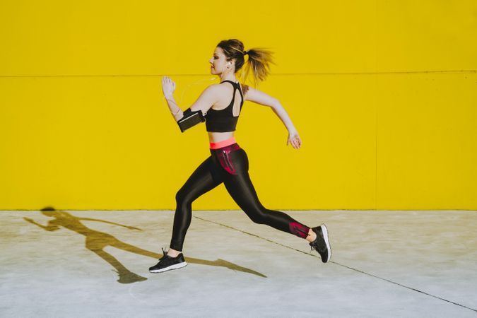 Woman with earphones running near wall