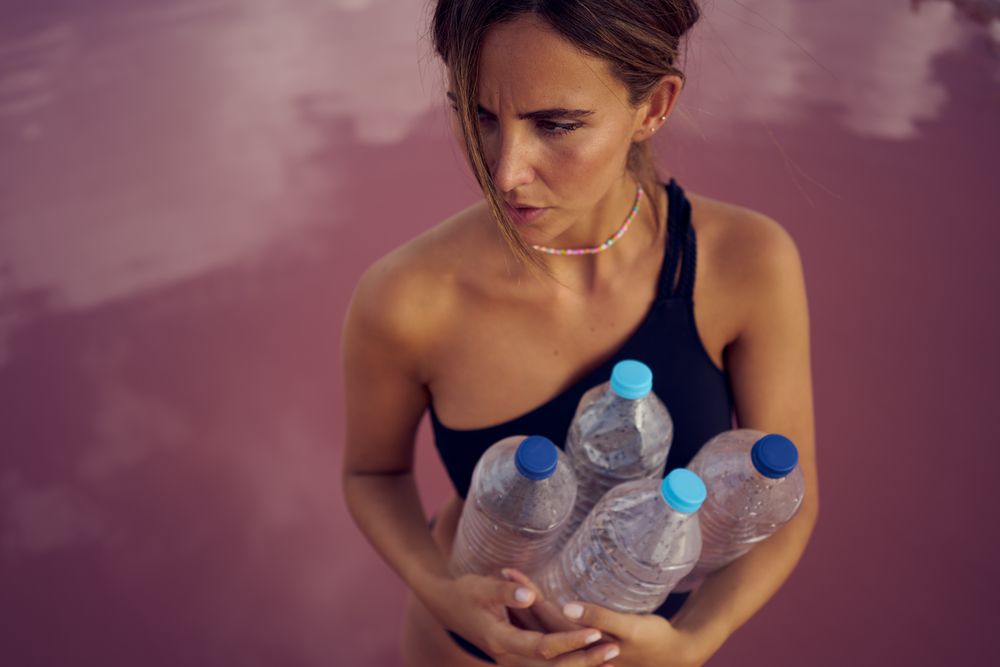Concerned female in swimsuit collecting trash in natural lake